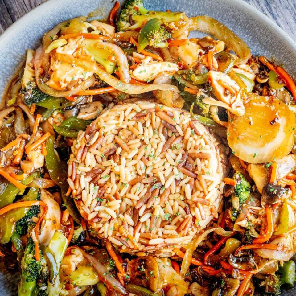 A close-up of a Mandee's Pizza stir-fry dish with rice, chicken, and colorful vegetables.
